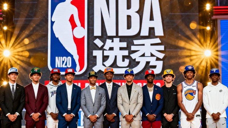 2025年NBA选秀大会现场，首轮新秀们站成一排合影，他们身着各自球队的帽子，背景是巨大的NBA选秀标志和聚光灯